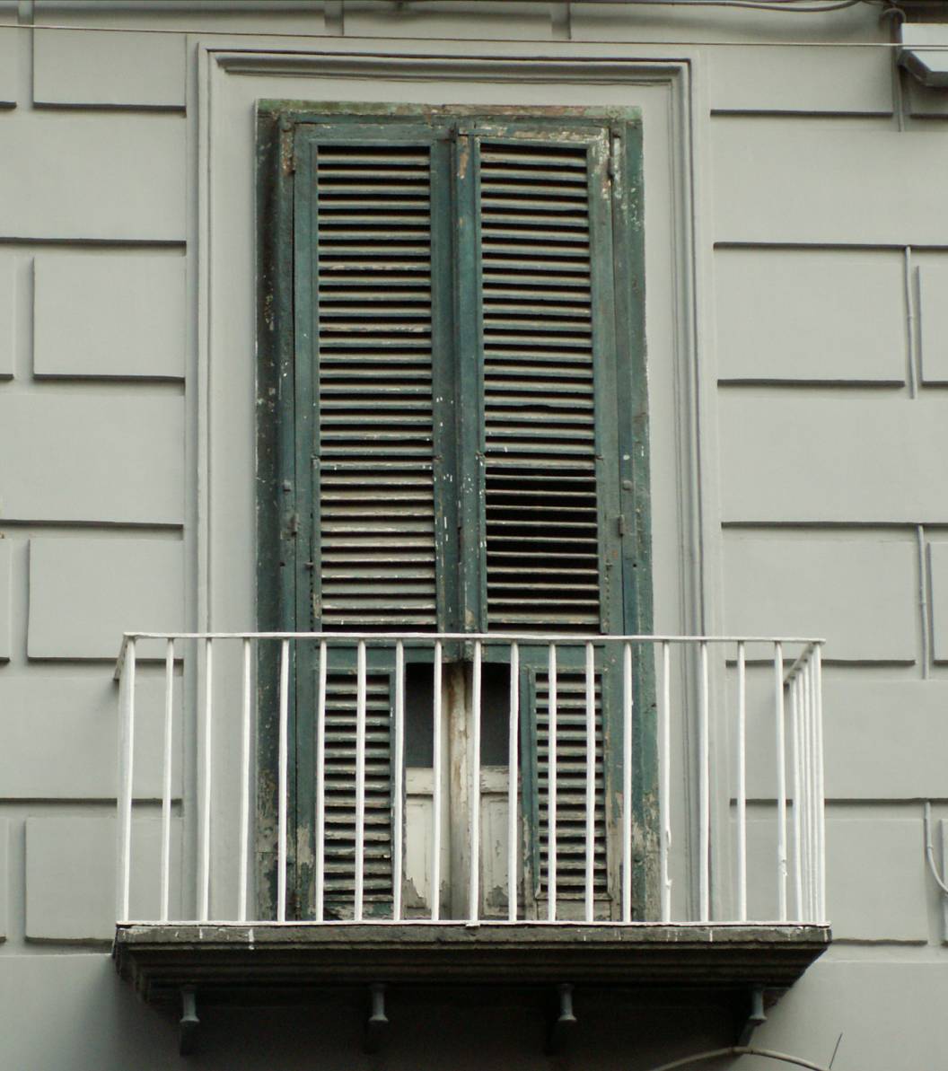 Napoli, edificio in via Roma, ringhiera, sollevata dal tavolone mediante dadi di spessore, con quadrelli paralleli alle spranghe, senza volute angolari (prima metà XIX sec.).