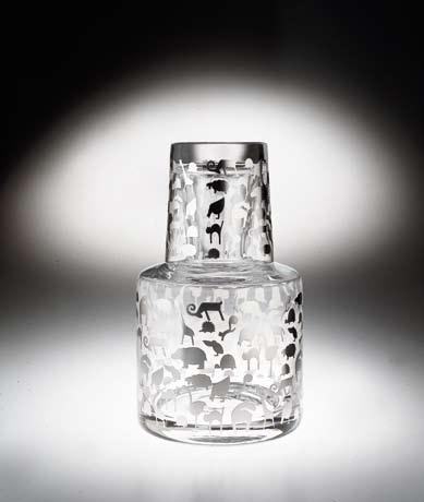 AIA M. Susani - E. Vidal, 1999 Servito da notte composto da bottiglia e bicchiere in vetro trasparente soffiato a bocca. Decorazione eseguita in serigrafia manuale con Argento 980/1000.