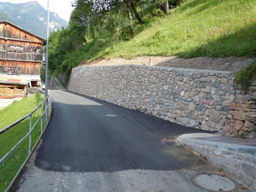 Fonesighe: realizzazione di un muro di sostegno in calcestruzzo rivestito in pietra per l allargamento verso monte della sede stradale, asfaltatura e ripristino delle aree.