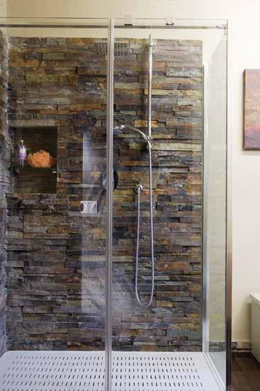 Nella stanza da bagno, la parete in intonachino color sabbia (Paletti Angelo) si interrompe nella cabina doccia, rivestita con pietre naturali a spacco.