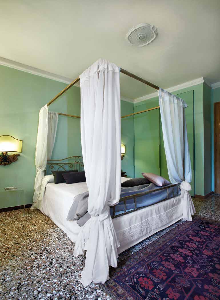 Nella camera degli ospiti, tra due applique d epoca spagnola, il letto a baldacchino, realizzato artigianalmente in ferro e ornato da tessuti di seta bianca.