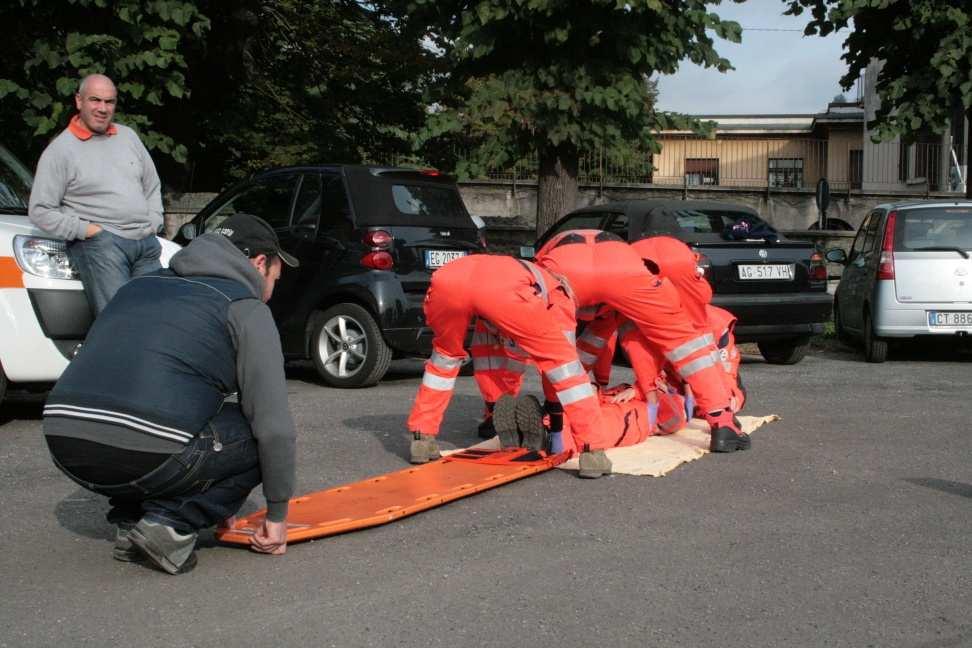 sollevano il paziente mentre un astante infila la tavola