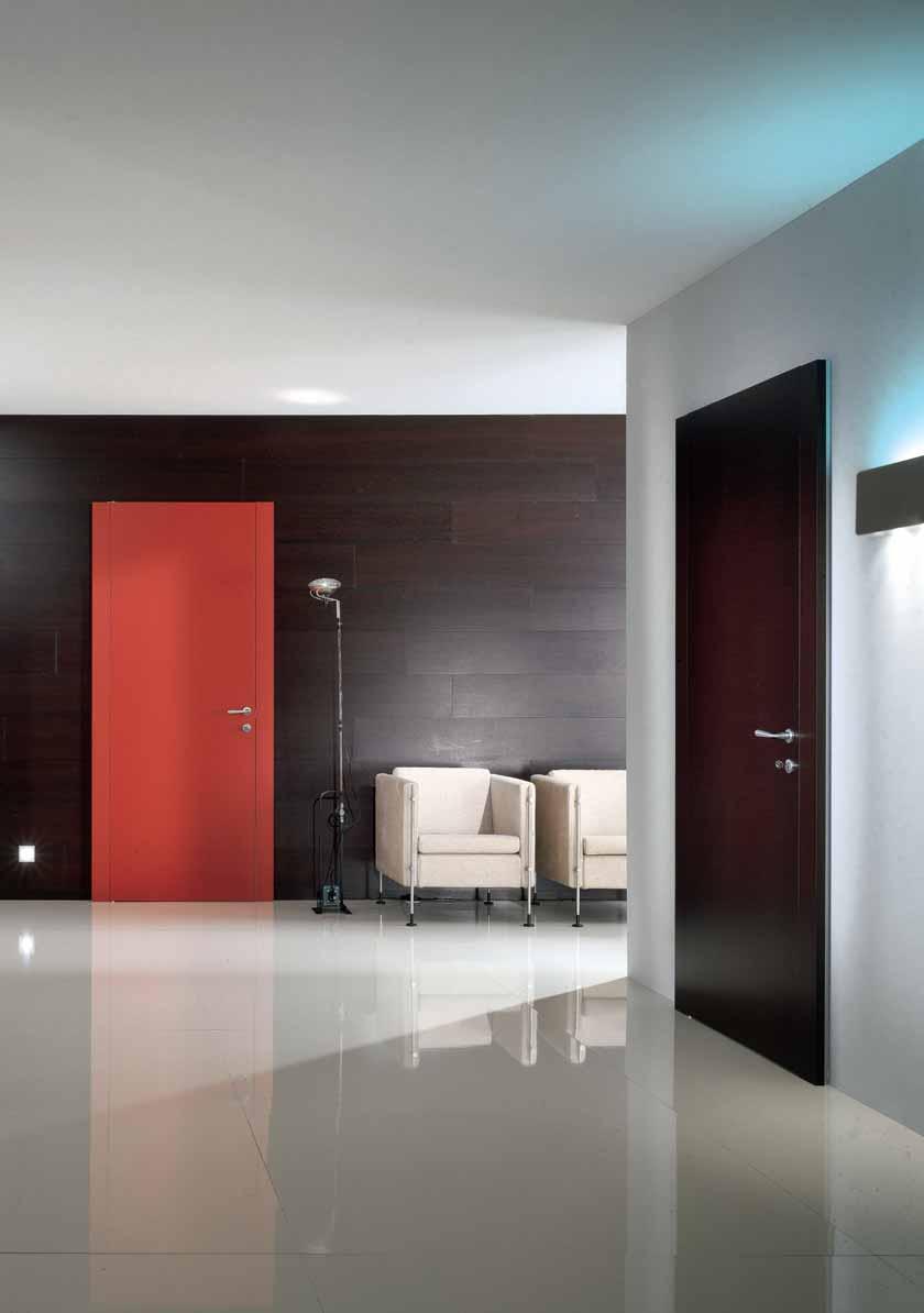 In fondo: sulla parete rivestita in legno scuro, si staglia la porta mod. Piana laccata Rosso china.