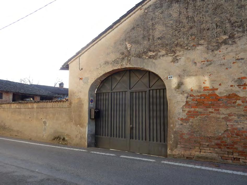 Muro continuo articolato su più livelli: da muro di recinzione diventa muro perimetrale del fienile interrotto da un portone di ingresso a forma di arco ribassato.