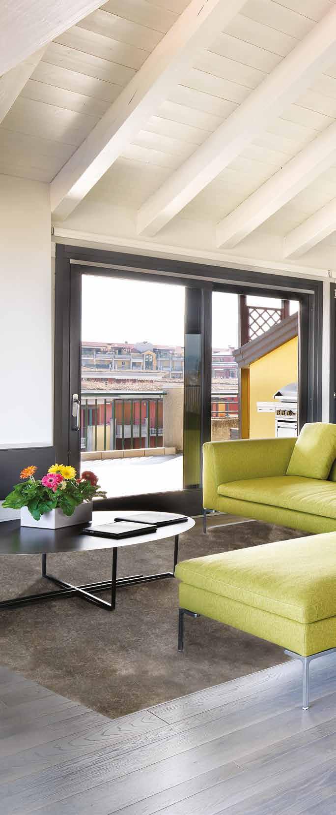 Affacciata su tre ampi terrazzi, la zona giorno è un arioso open space che gli arredi moderni suddividono nelle aree del living, con divano in tessuto giallo lime e tavolo da pranzo con piano in