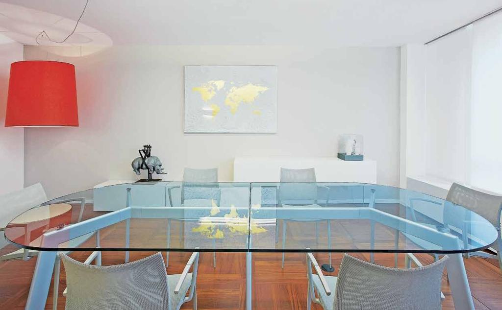 Nel centro della stanza tavolo ellittico, in vetro, di Desalto. A parete moduli bianchi Lago con finiture in vetro lucido per custodire le pratiche lavorative.