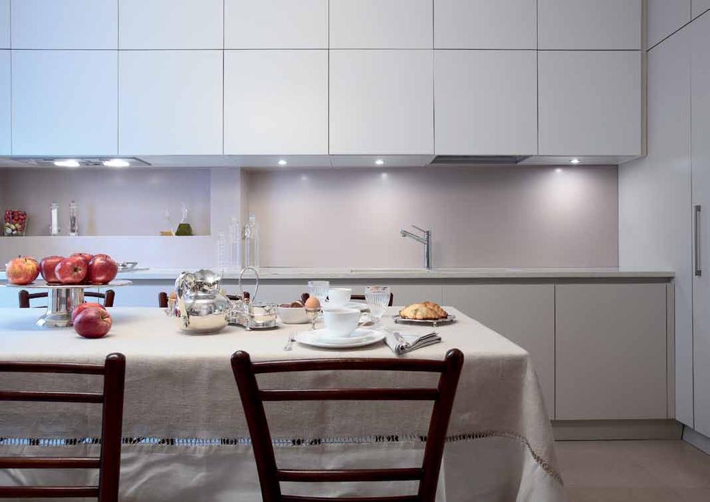La cucina laccata opaca è realizzata su disegno delle progettiste (Contini e Donati Architetti, Brescia) e si snoda regolarizzando la parete di fondo con un piano a due profondità in marmo bianco.