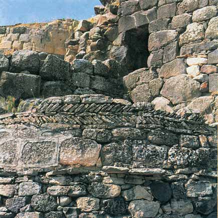 Fig. 62 Barumini, Su Nuraxi. In primo piano, particolare del fregio a spina pesce del vano zz; sullo sfondo l ingresso sopraelevato al nuraghe (Fase c).