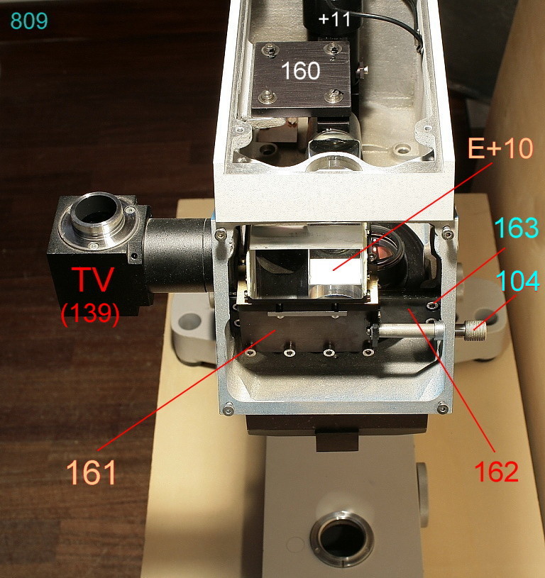 Fig. 1068 Visto di fronte, il braccio mostra il carrello 161 per la traslazione dei prismi visione-foto (E+10). Il carrello è mosso da un asta che sporge esternamente col pomello 104.