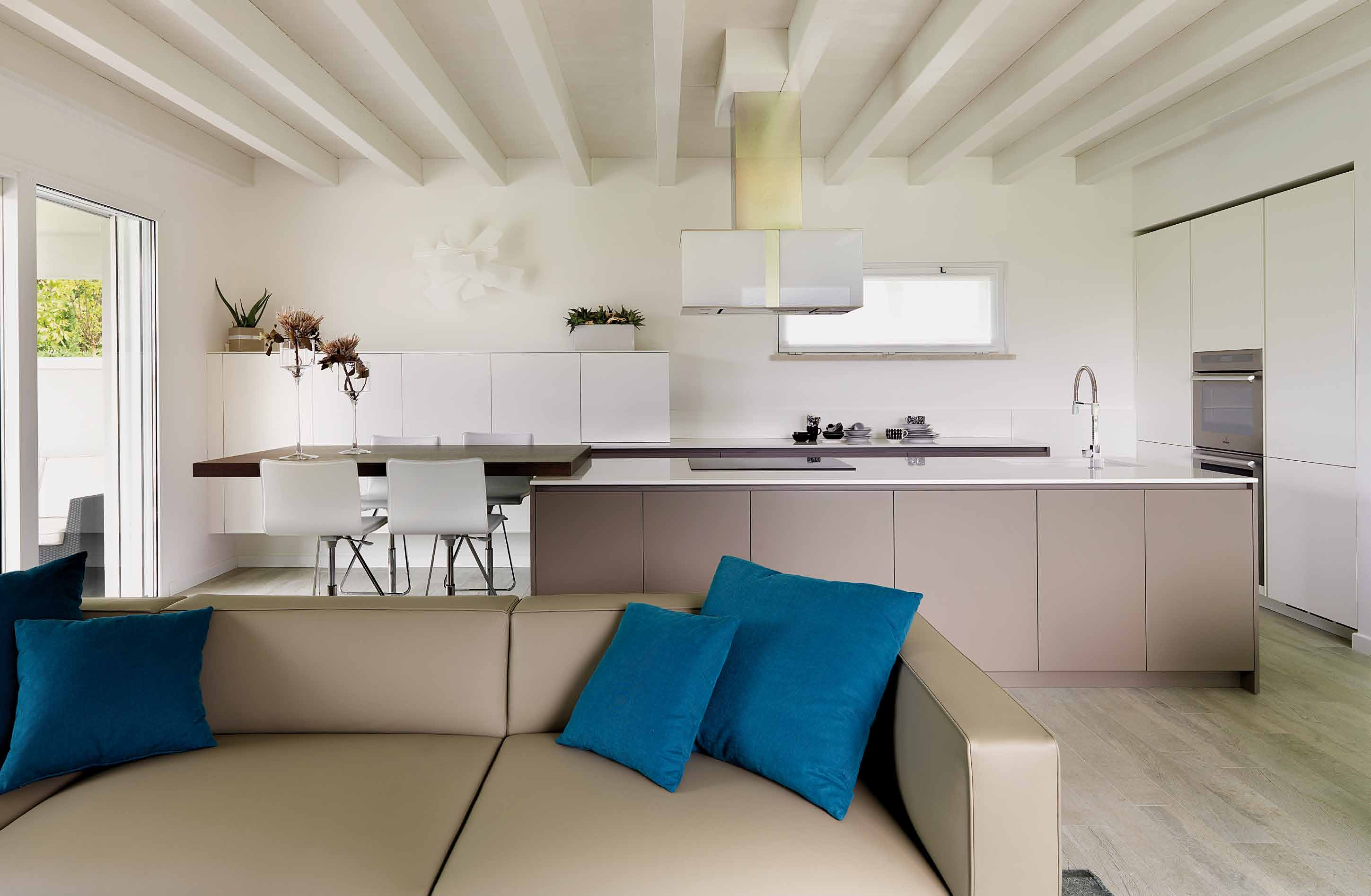 Organizzata e funzionale, la cucina laccata bianco opaco e tortora ha ampio sviluppo: lungo la parete, serie di mobili contenitori e area lavoro, con piano in Okite bianco assoluto.
