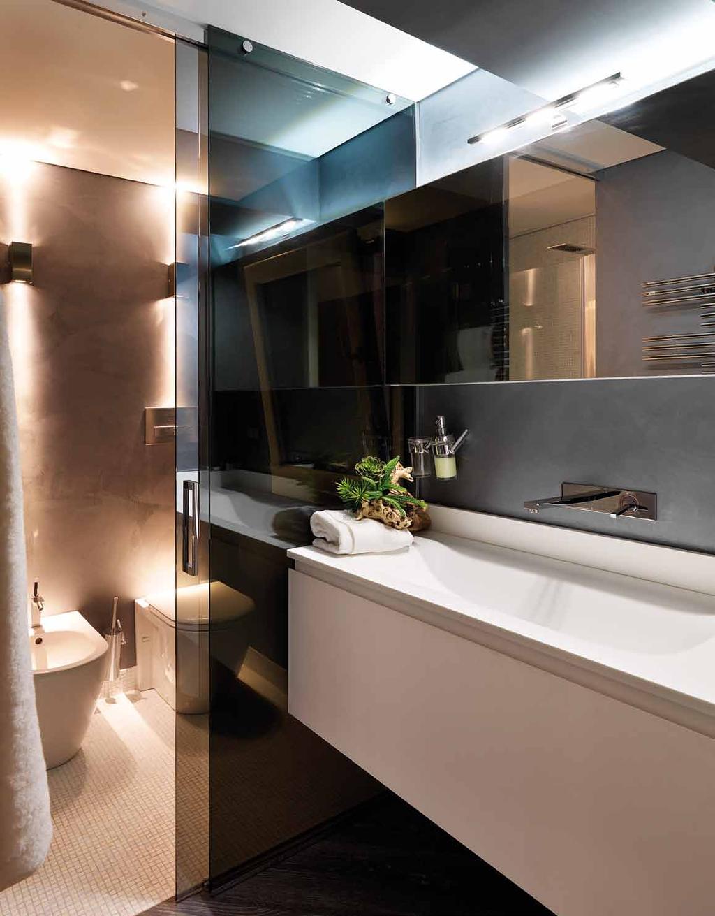 Elegante bagno padronale suddiviso in due settori da una porta scorrevole in cristallo Stop sol: nella zona dei sanitari e della doccia rivestimenti e pavimentazione in mosaico bianco; nella zona
