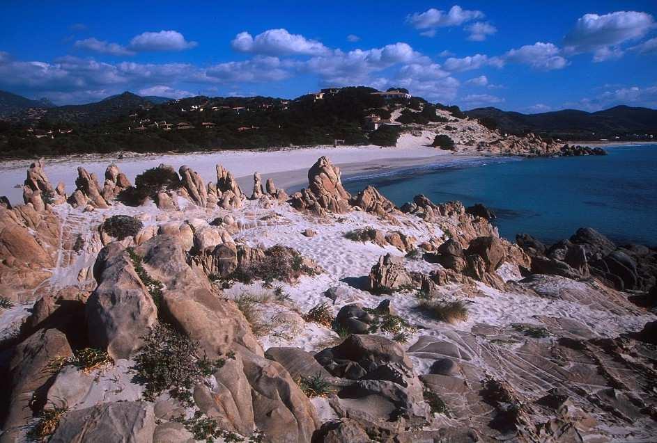 Spiaggia di Timi Ama Osservandola da Punto Giunco, Timi Ama offre un profilo stupendo. Le alte montagne sovrastano una pineta e le dune di sabbia bianca, dove lo sguardo si immerge nel mare turchese.