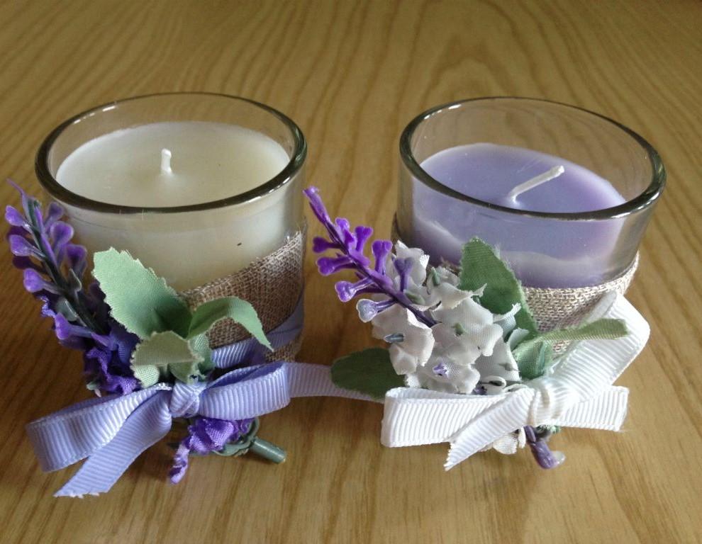 Le Candele alla Lavanda sono composte da un bicchiere in vetro adornato con un tessuto e decorazioni floreali a tema lavanda.