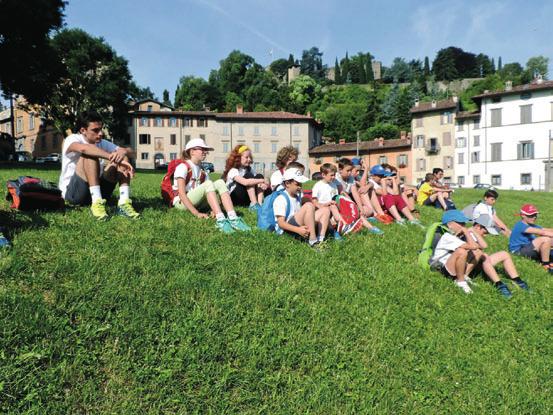 Una trentina di Aquilotti di Bergamo sono seduti sul prato verde della Fara, di fronte alla ex chiesa di San Agostino in Città Alta, con lo sguardo rivolto agli Accompagnatori di Alpinismo Giovanile