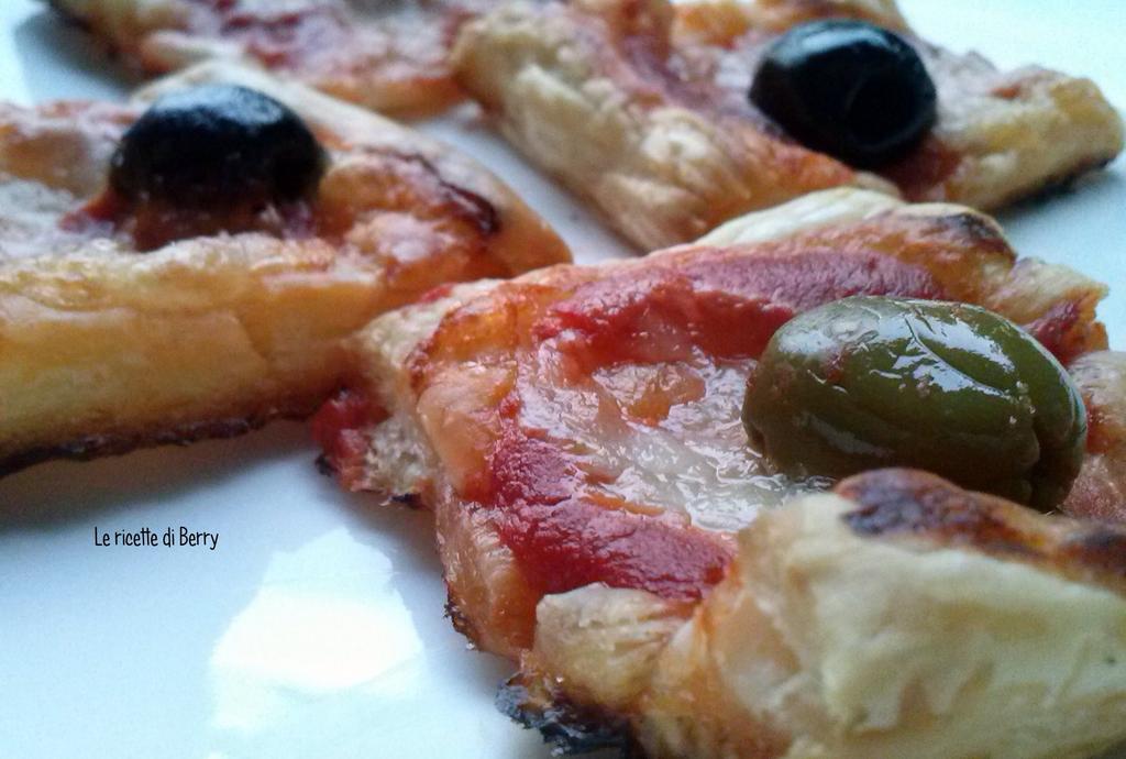 Pizzette di Pasta Sfoglia alle Olive 1 rotolo di pasta sfoglia rettangolare 150 ml di passata i pomodoro 16 olive 1 mozzarella origano q.b.
