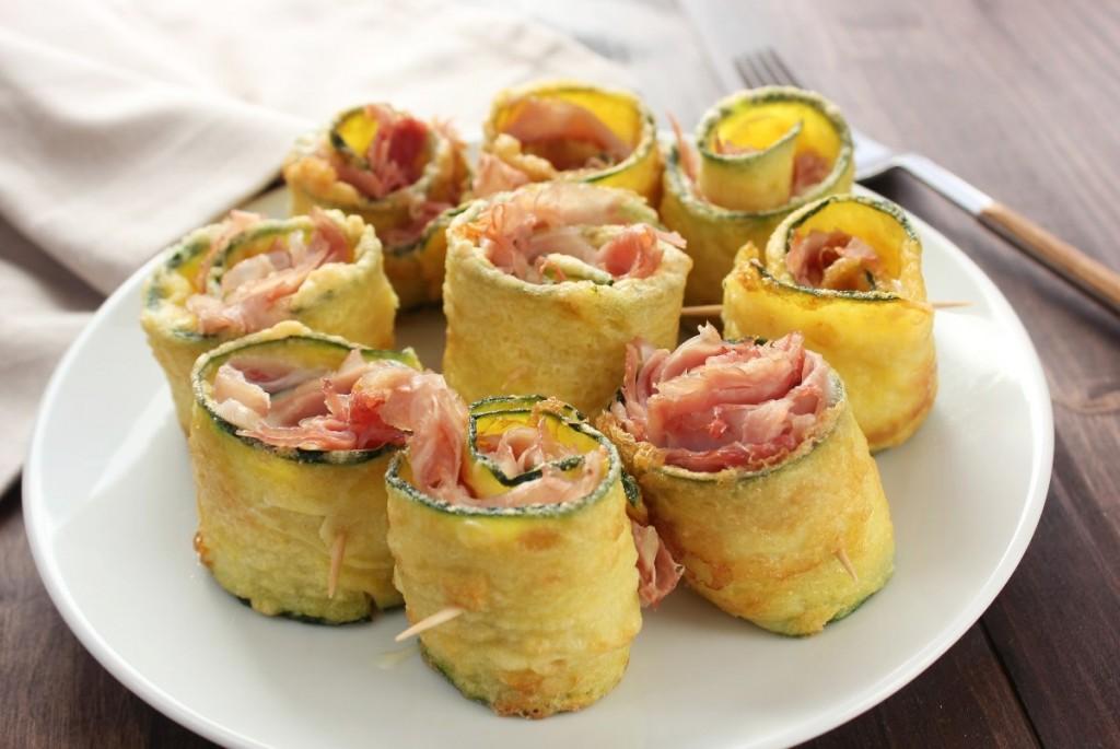 Gli involtini di zucchine fritte ripiene di prosciutto cotto e formaggio filante sono una vera delizia, ideali per un antipasto, un aperitivo, ma sono ottimi anche da servire come un secondo piatto.